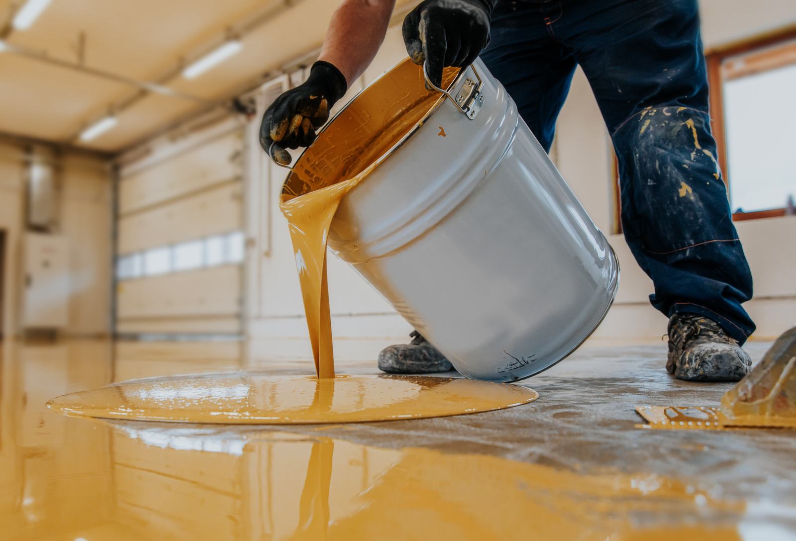Installer pouring amber epoxy coating from a bucket onto a concrete floor